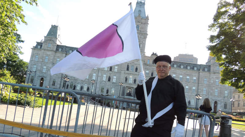 Devant le parlement du Québec avec le drapeau de la fierté ronde.