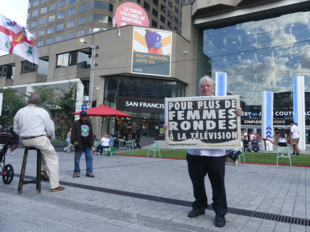 Jos Breton devant l'entre du Complexe Desjardins  Montral manifestant sur la rue Ste-Catherine pour plus de femmes rondes  la tlvision au gala des prix gmeaux 2025.