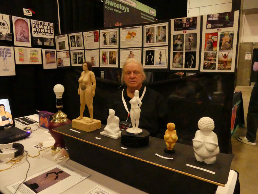 Jos� Breton assis avec ses artefacts vu de face : poup�e barbie ronde, Shekinah, Ginette, V�nus de Willendorf, version de la V�nus de Willendorf